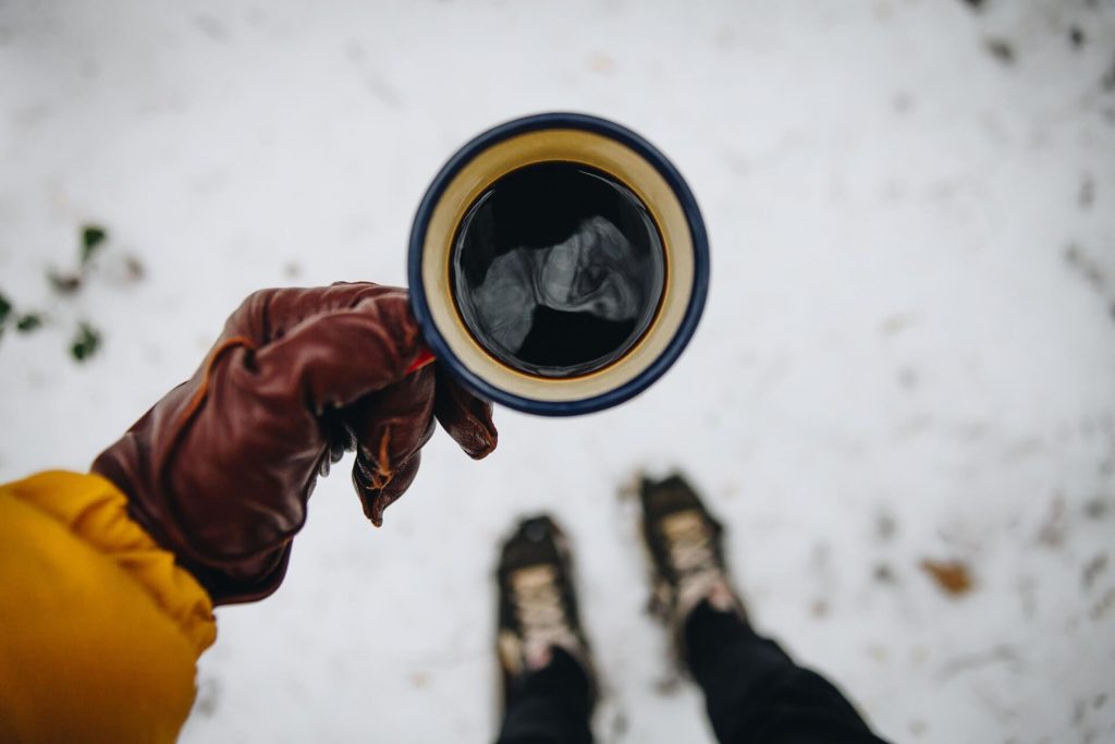 Personne dégustant une tasse de café dans un paysage arctique enneigé.